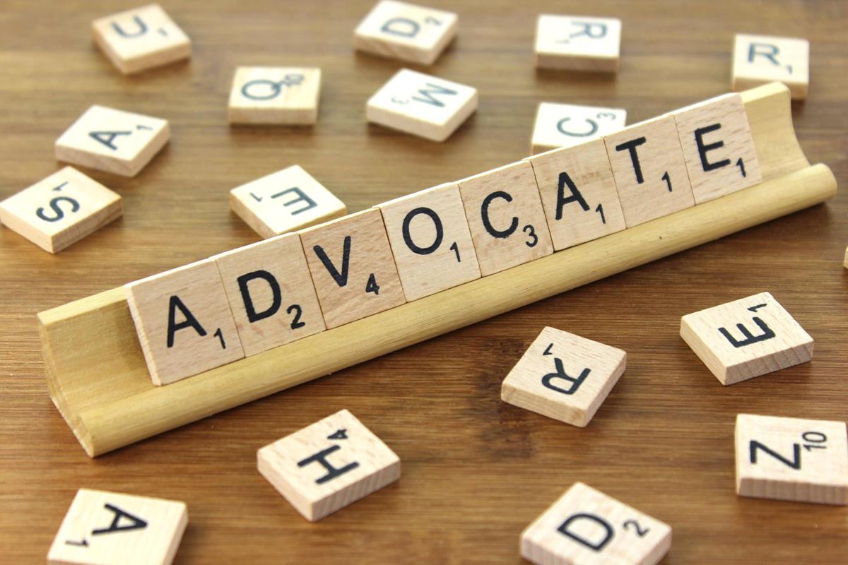 Advocate spelled out in Scrabble tiles with other tiles laying around the word.